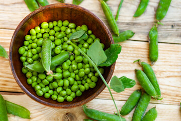 closeup green peas in brown dish, on wooden table.