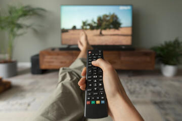 Fototapeta Woman watching TV at home and holding the remote control obraz