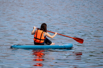 Sup surfing, girl in life vest sitting with paddle on a board in water. Paddleboarding in summer