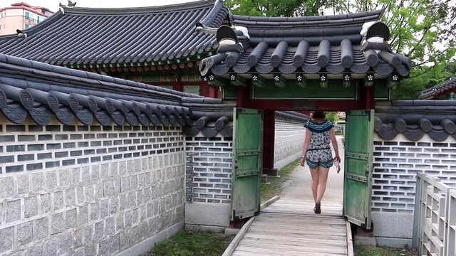 Seoul historic palace - woman traveller walking through a small gate in the wall.