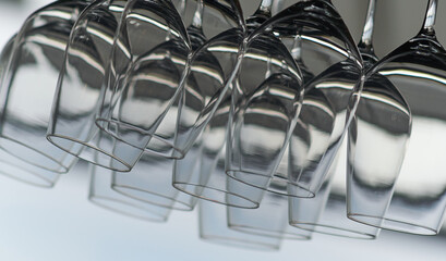 Close up detail view of many empty wine glasses hanging upside down on a special rack over the counter of a bar.
