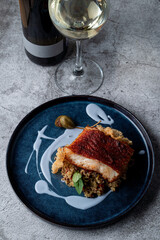 Fried fish fillet with golden crust and a glass of white wine on a restaurant grey table