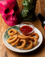 Golden deep fried onion rings with tomato chili sauce on a wooden table, modern decorated bar