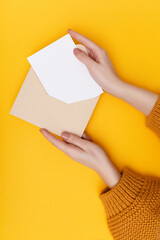 Biege envelope with blank white postcard in woman's hands on the yellow background. Mail concept
