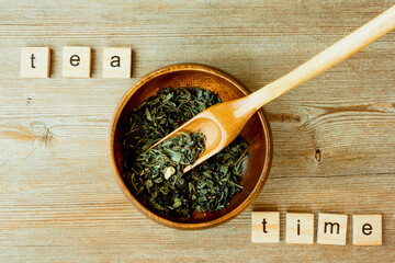 Tea time inscription, Chinese, Japanese green dried tea leaves at bamboo scoop and bowl on table
