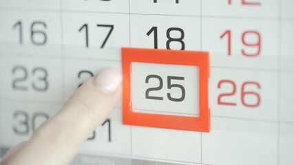 Woman's hand in office changes date at wall calendar. 25