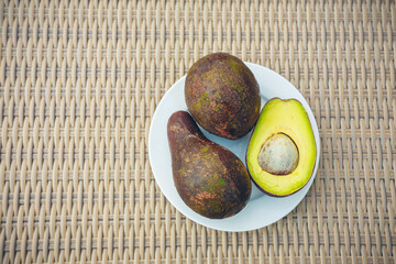 Ripe sliced and whole avocados on white plate on wicker background