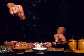 The chef of the restaurant sprinkles with curry spices and basil meat on a black background. Marinating pork for barbecue and ham.