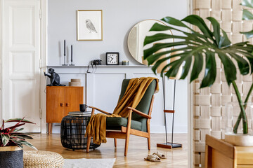 Stylish interior of living room with design armchair, wooden vintage commode, round mirror, shelf, tropical leaf, coffee table, decoration, carpet and persnoal accessories in home decor.