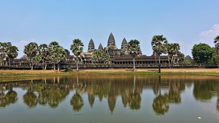 Fototapeta na wymiar The famous temple of Angkor Wat. In the foreground is a lake, in the distance, against a clear blue sky, the ruins of an ancient palace with towers, galleries, colonnades. Reflection in water. UNESCO