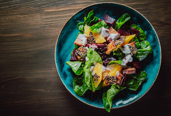 vegetarian salad with beets, spinach, orange, tofu in plate on wooden table background