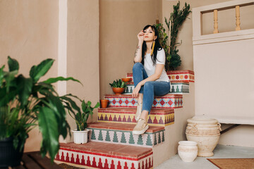 A beautiful young Asian brunette girl in jeans and a white t-shirt is sitting on the steps with a pattern .