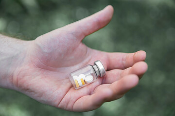 The person holds a closed bottle with tablets in his hand