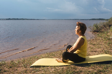 Senior woman making yoga near river.
