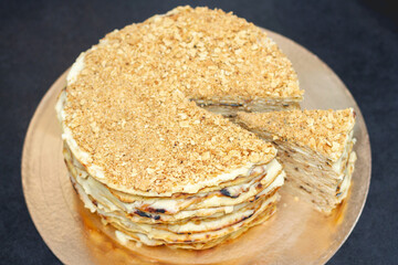 layer cake with cream, sprinkled with crumbs on a black table. one piece of the pie has already been cut off