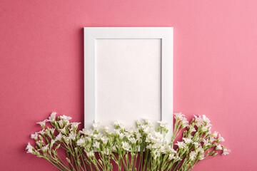 White empty photo frame mockup with mouse-ear chickweed flowers on pink purple background, top view copy space