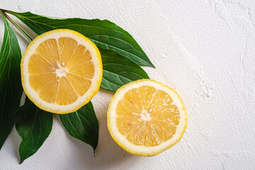 Two lemon slices, tropical citrus fruits with green leaves on white concrete background, top view macro