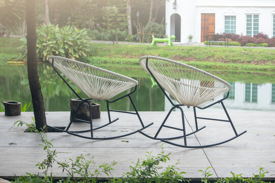 Two White Rocking Chair On The Backyard In Tropical Garden Near Lake,two Empty White Rocking Chair,there Are No People Around.Spring Morning By The Lake,The Concept Of Loneliness, Relaxation.