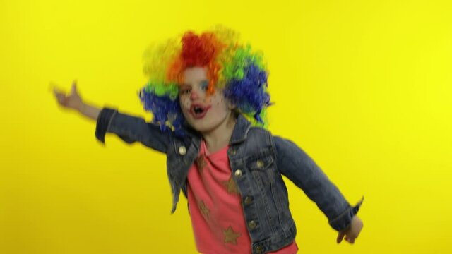Little Child girl clown in colorful wig making silly faces. Having fun, smiling, dancing. Halloween