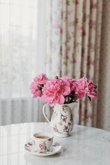 pink peonies on the table with a cup of tea