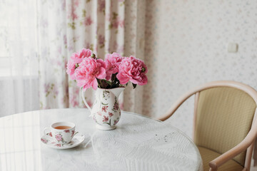 pink peonies on the table with a cup of tea