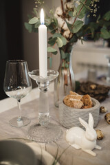burning candle in a candlestick next to glasses and a glass rabbit