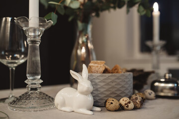 burning candle in a candlestick next to glasses and a glass rabbit