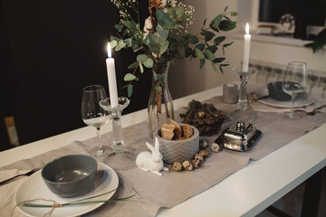 burning candle in a candlestick next to glasses and a glass rabbit