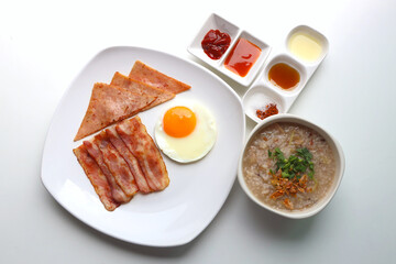 Rice Porridge, ham, bacon, fried egg, served with various sauces Put on the white table Ready to eat