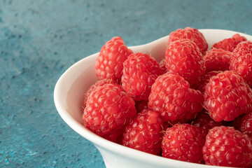 ripe raspberry fruits in a bowl on blue background