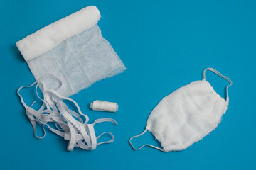 Gauze mask, bandage, threads, needle, rubber on blue background. Manufacture of protective surgical mask with your own hands, DIY mask material. Respiratory coronavirus protection. Isolated