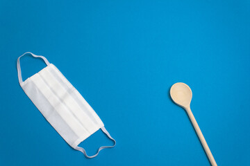 Concept protective equipment vs pandemic, coronavirus, top view. Medical, hygiene, reusable, cotton face mask, wooden spoon on blue background, isolated. Blank space for text