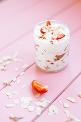 layered summer dessert with strawberries, sponge cake and yogurt on a pink tree background.