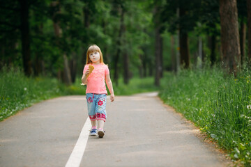 A little girl walks along the path in the summer park and holds an ice cream cone in her hands