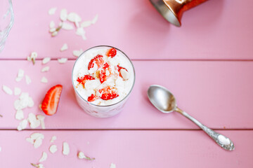 layered summer dessert with strawberries, sponge cake and yogurt on a pink tree background.