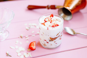 layered summer dessert with strawberries, sponge cake and yogurt on a pink tree background.