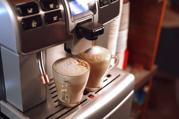 two delicious hot cups of cappuccino are in the coffee machine for lunch