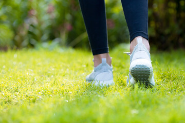 Runner legs running on a green lawn closeup on shoes. Fitness woman sunrise jogging workout welness...