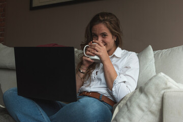 happily woman working on the couch from home with a coffee