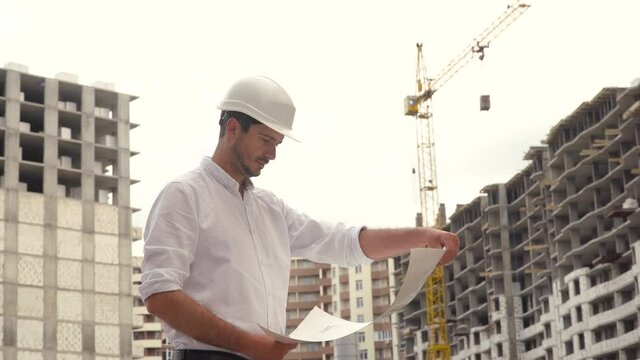 Architect or engineer working in hard hat browsing building project of construction site with blueprint plan