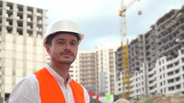 Portrait of a successful young engineer, architect, builder, businessman, wearing a white helmet, in a shirt on a construction site