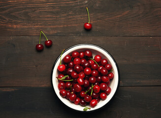 ripe red cherry in a round metal bowl on a brown wooden background