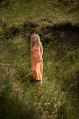 girl in a linen orange dress with dry flowers in her hands in a green ravine