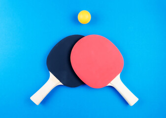 directly above shot of two table tennis rackets and ball on blue background.