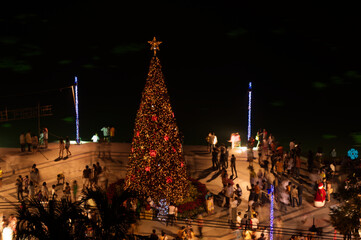 Blur image of Asian people celebrating Christmas party or new year festival around Christmas tree in the open space by the river at night