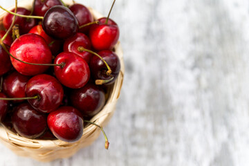 Ripe cherry berries in the basket on the wooden background. Top view. Selective focus