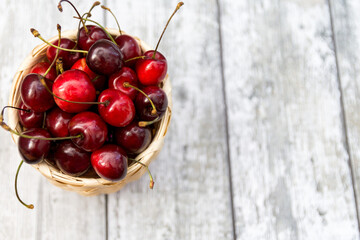 Ripe cherry berries in the wooden basket on the wooden background. Top view with selective focus