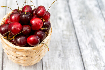 Ripe cherry berries in the basket on the wooden background. Selective focus