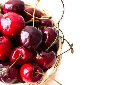 Closeup phote of ripe cherry berries in the wooden basket isolated on the white background. Copy space. Top view with selective focus