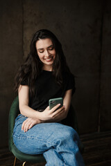 Photo of beautiful smiling woman sitting on chair and holding cellphone